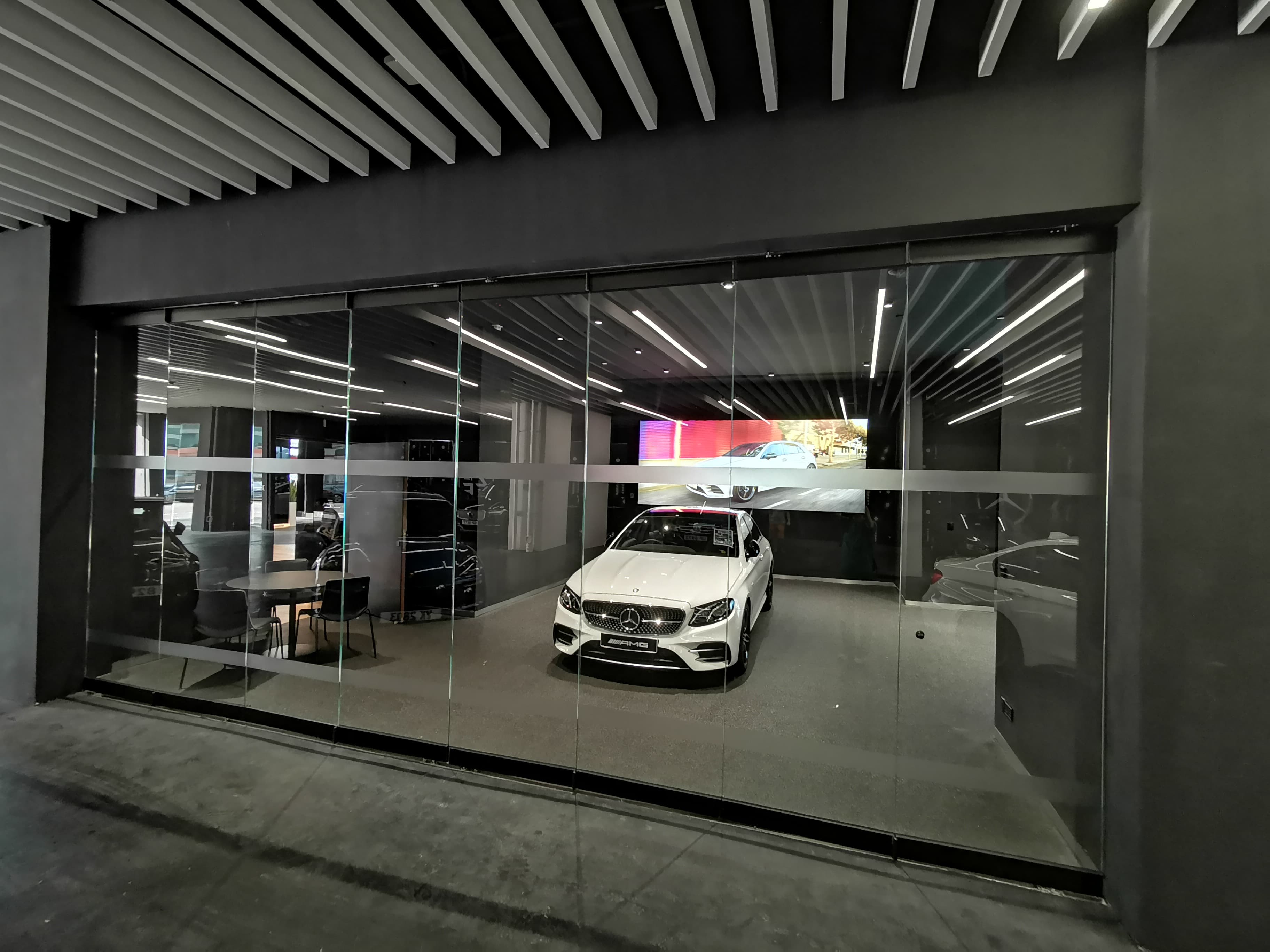 现代玻璃展厅内停放着一辆白色梅赛德斯-奔驰 AMG,上方是条纹天花板。