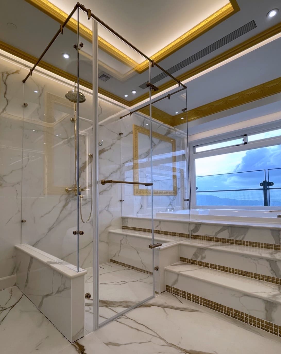 Baño de lujo en mármol con detalles dorados y cabina de ducha de vidrio.